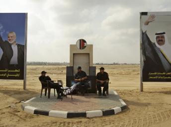 Des membres des forces de sécurité du Hamas patientent devant les portraits du leader de leur mouvement et de l'émir du Qatar.